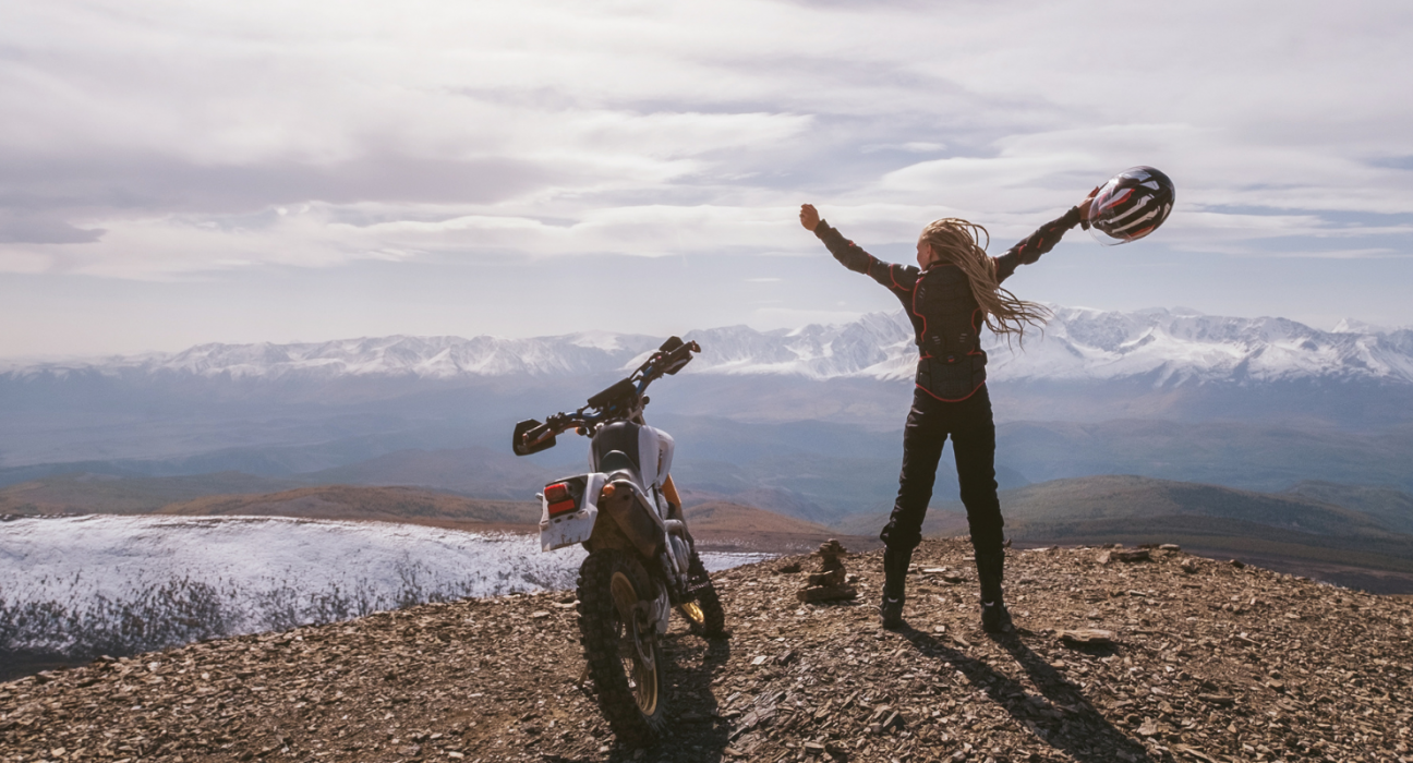 female motorcyclist standing on top of mountain holding helmet