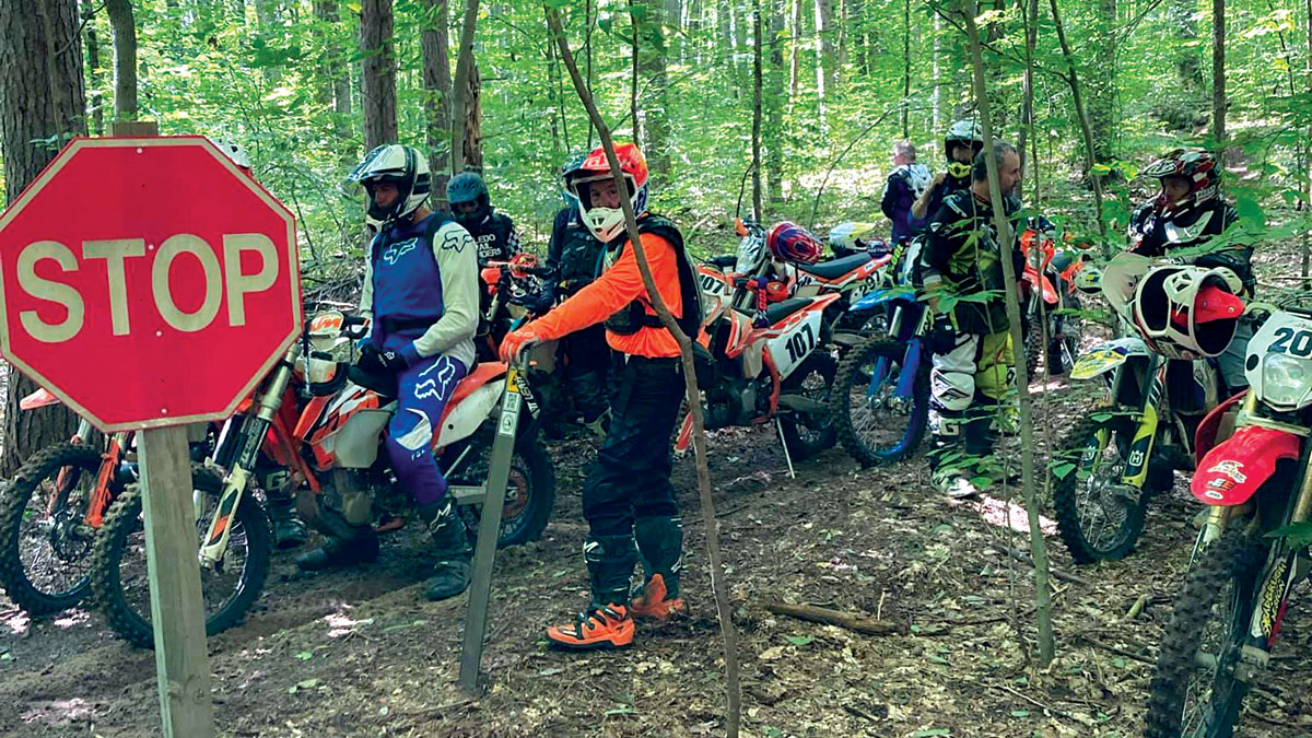A group of motorcycle riders taking a break on a forest trail next to a stop sign.